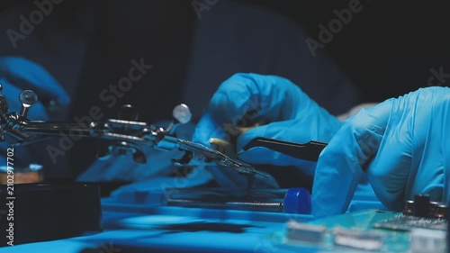 Technician inspecting a circuit board with a magnifying glass. Close up of hands in blue gloves working on microelectronics in a laboratory.