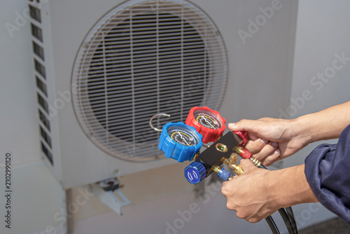 Air conditioning, HVAC service technician using gauges to check refrigerant and add refrigerant.