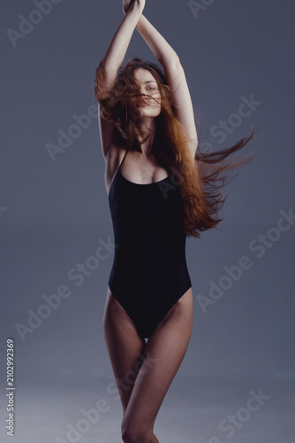 Canvastavla slender woman in black bodysuit dancing with arms raised against gray background