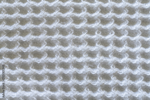 A close-up shot shows a white knitted fabric with a repeating wavy pattern. The texture appears soft and slightly raised, creating a dimensional effect.