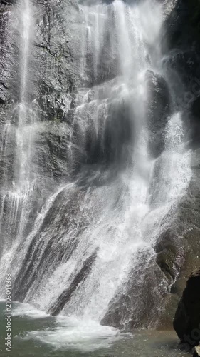rushing white waterfall spills over dark sculpted rocks into a clear pool, revealing sparkling spray, wet textures and powerful freshwater movement in a wild forest