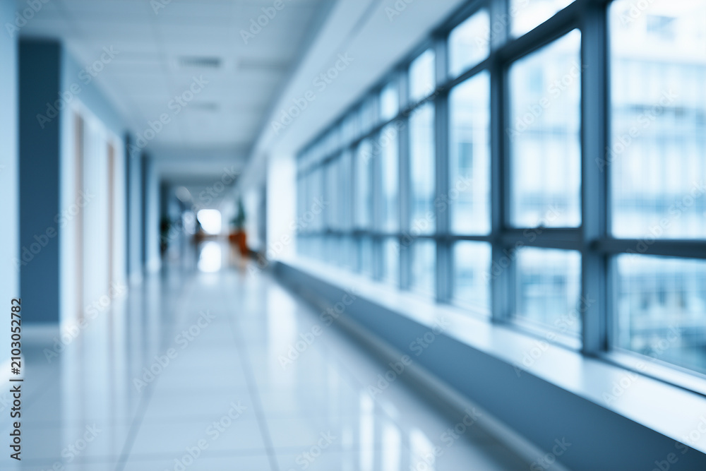 Fototapeta premium Blurred view of a long modern office corridor with large windows and reflective floor