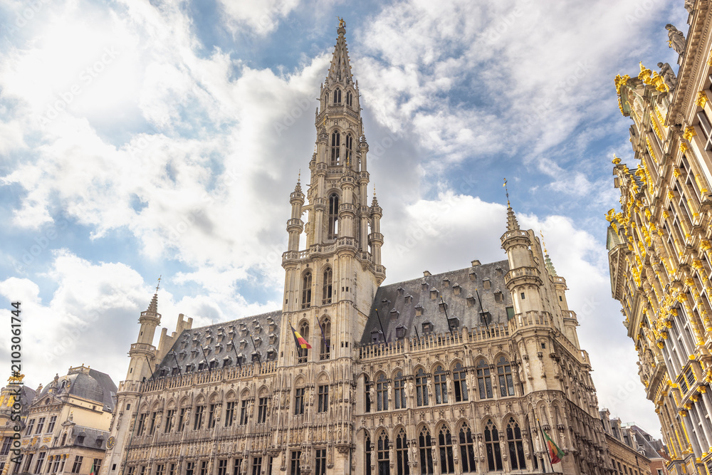 Fototapeta premium City of Brussels in Belgium, Europe. The Town Hall in Grand Place Square, historic European architecture under a bright blue sky with white clouds, showcasing intricate details and classic design
