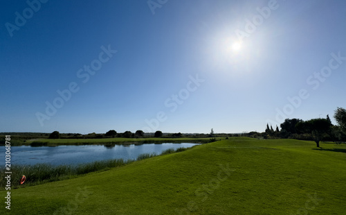 Schilderij op canvas Vibrant green golf course landscape with mature trees under a clear blue sky