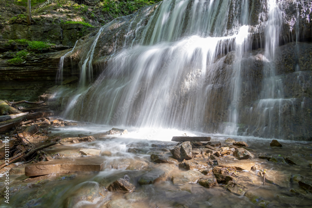 Fototapeta premium Serene view of Sherman Falls cascading over rocks in Hamilton, Ontario, surrounded by lush greenery.