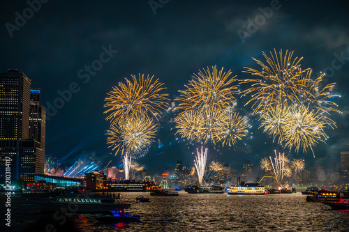 Fourth of July celebration fireworks over New York City. Bright golden bursts and vertical trails rise from barges near Manhattan skyscrapers.