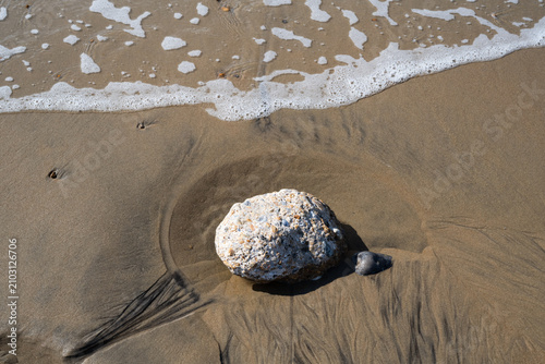 Foto Conglomerate rock on wet beach sand with tidal drainage patterns