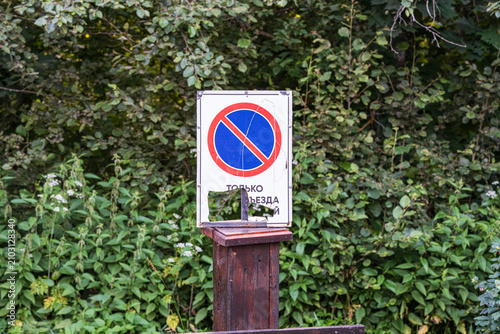 Schilderij op canvas A damaged road sign, indicating for passing vehicles only, stands amidst dense greenery