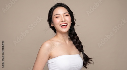 young woman with long dark braided hairstyle, natural makeup, wearing a white strapless tube top, jumping joyfully, laughing happily, isolated on a beige seamless studio background