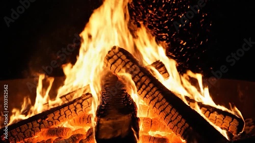 Bright orange flames burn through wooden logs in a campfire
