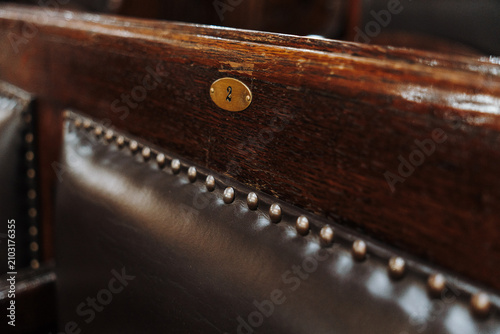 Photography Close-up of a numbered wooden bench with leather upholstery in a historic interior