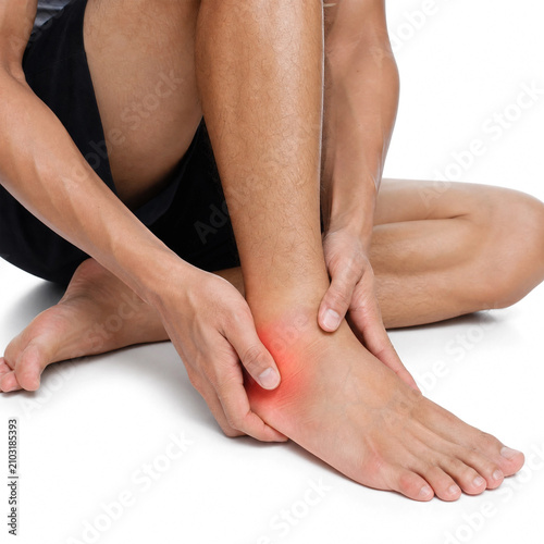 Man experiencing acute ankle pain holding his injured foot with both hands on a plain white background