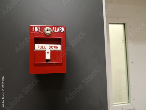 Fire alarm pull station on a wall, red emergency device with warning labels, concept of building safety and fire protection.