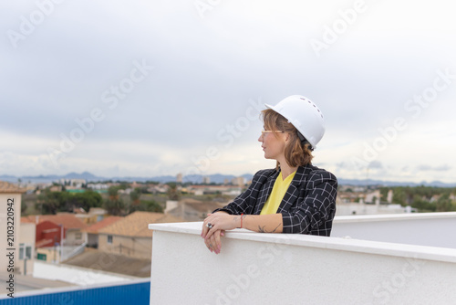 Fotografie Woman civil engineer or architect wearing a hardhat and glasses observing an urb