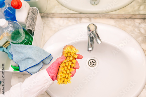 Close-up of pink-gloved hand holding a yellow sponge over a bathroom sink