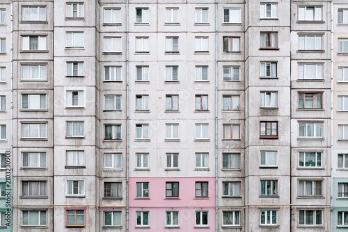Concrete apartment building facade with repetitive balconies and windows, highlighting minimalist residential architecture and the uniform rhythm of an aging urban neighborhood.