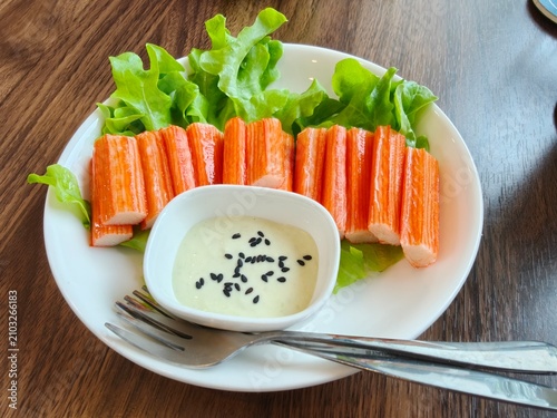 Imitation crab sticks served with salad cream dressing and fresh green oak lettuce on a white plate