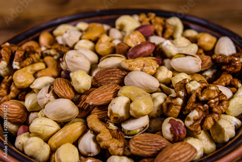 Various nuts (almond, cashew, hazelnut, pistachio, walnut) in ceramic plate on a wooden table. Vegetarian meal. Healthy eating concept