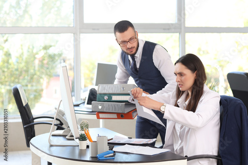 Angry female boss tearing paper with male employee at desk in office