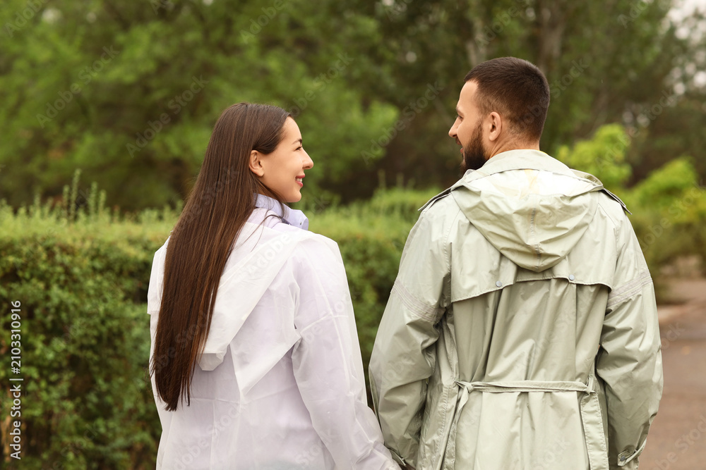 Fototapeta premium Young couple with raincoats in park, back view