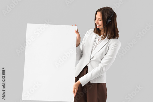 Female technical support agent with blank poster on light background