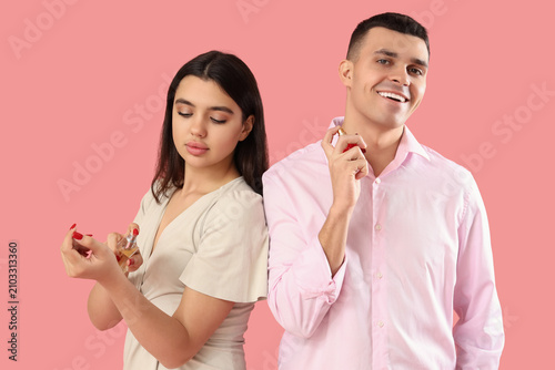 Young couple applying perfume on pink background