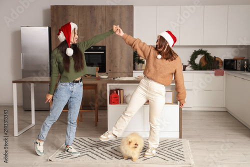 Young lesbian couple with Pomeranian dog dancing in kitchen on Christmas eve