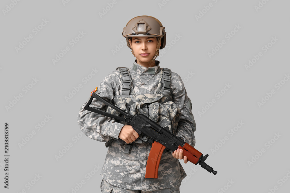 Fototapeta premium Confident young female soldier with assault rifle on grey background