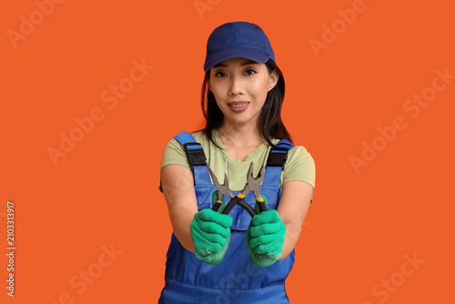 Young female electrician with pliers on orange background