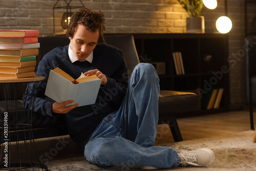 Young man reading book at home late in evening