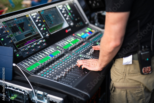 Close-up of an audio engineer adjusting a professional digital mixing console during a live music performance at an outdoor concert venue.