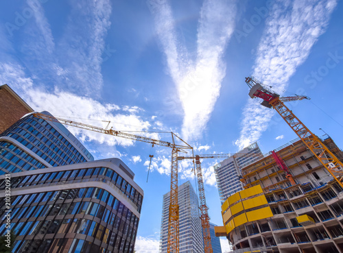 Construction cranes work in city center. Cranes stand tall against a blue sky as workers build new structures in a busy city center during the day.