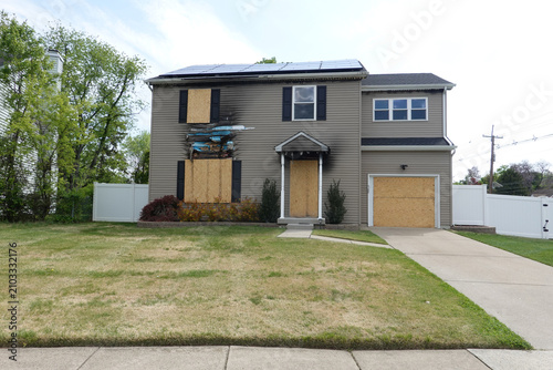 Abandoned fire damaged house with boarded windows and and doors with solar panels on roof in suburban setting