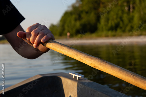 Fotografía Close-up of a rower's hand gripping a paddle on an old boat during a sunset ride across a peaceful lake