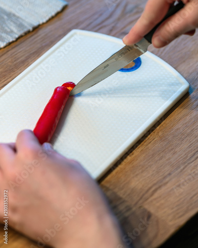 Fotografía Knife cutting end of long red pepper on white board