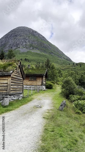 Traditional Norwegian houses with iconic grass-covered roofs nestled beside a crystal-clear mountain stream flowing down from the mountains. Surrounded by lush greenery and breathtaking Scandinavian l