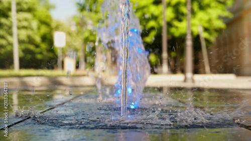 Ground-level fountain jet spraying water on city pavement, refreshing urban summer scene with reflections, 4K