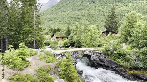Powerful mountain river rushing beneath a historic stone bridge, surrounded by majestic mountains and pristine Norwegian wilderness. Crystal-clear water, rugged rocks, and breathtaking Scandinavian sc