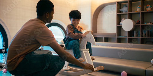 Fotografía Father playing with son on rocking horse in modern children's playroom