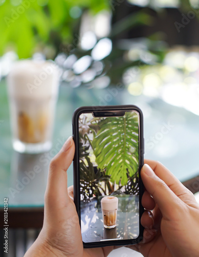 Person Photographing Iced Coffee with Smartphone in Tropical Café for Social Media