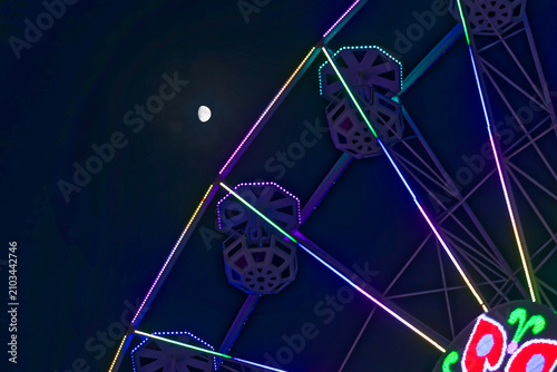 фотографія Ferris Wheel Illuminated with Vibrant Lights Under a Bright Moon at Night