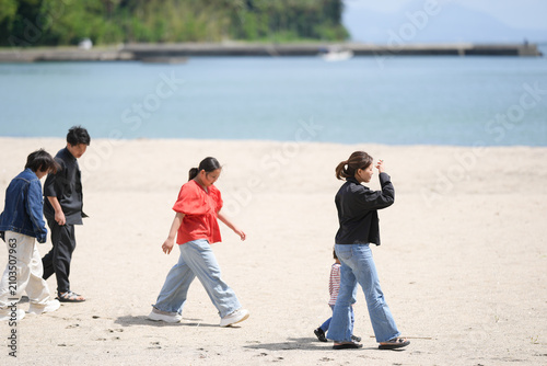 Fotografía Four people stroll barefoot on a wide, sunlit beach