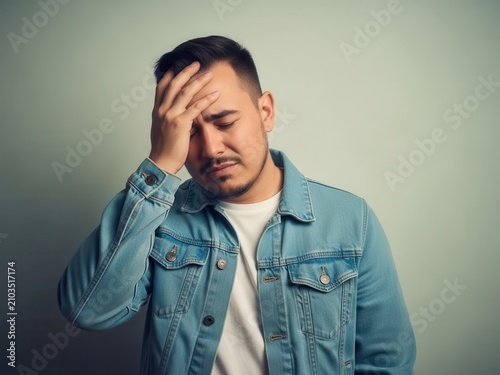 Stressed young man touching his head looking frustrated and disappointed in a casual denim jacket