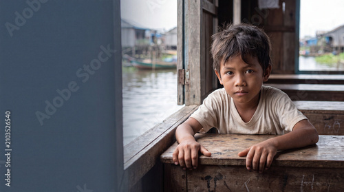 Close-up of a local Southeast Asian boy at a wooden desk by the window in a floating classroom, concept of global climate change and education equity with water copy space