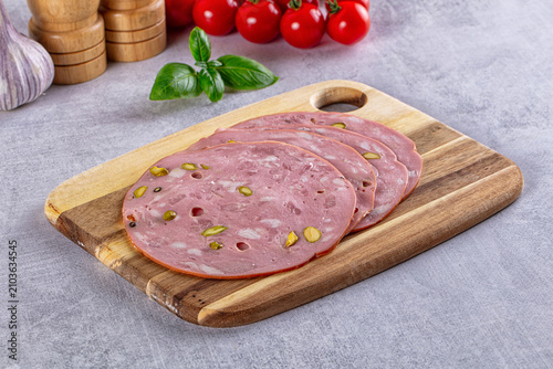 Sliced mortadella with pistachios on wooden cutting board