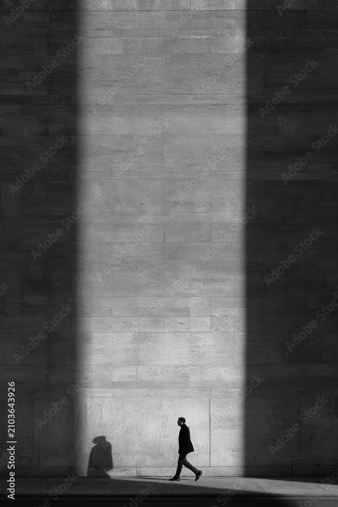 Fototapeta premium Dramatic shadow play shows a person walking past a textured wall during the day with clear outlines of shadows cast on the surface