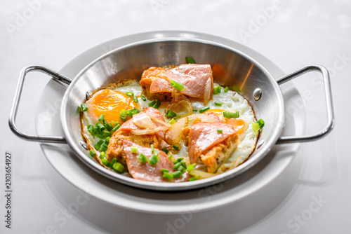 Close up of pan fried eggs topped with ham, sauteed onions, and chopped green onions served in a stainless steel skillet. Delicious Asian breakfast concept. Food close up.