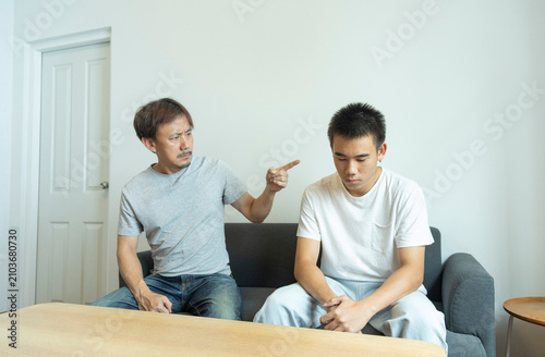Canvas Print Asian father scolding his teen son in casual white T- shirt in light white modern interior living-room