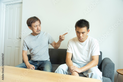 Konstfotografi Asian father scolding his teen son in casual white T- shirt in light white modern interior living-room