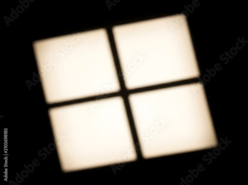 Four glowing square windows light panels arranged in a grid pattern against a dark black wall